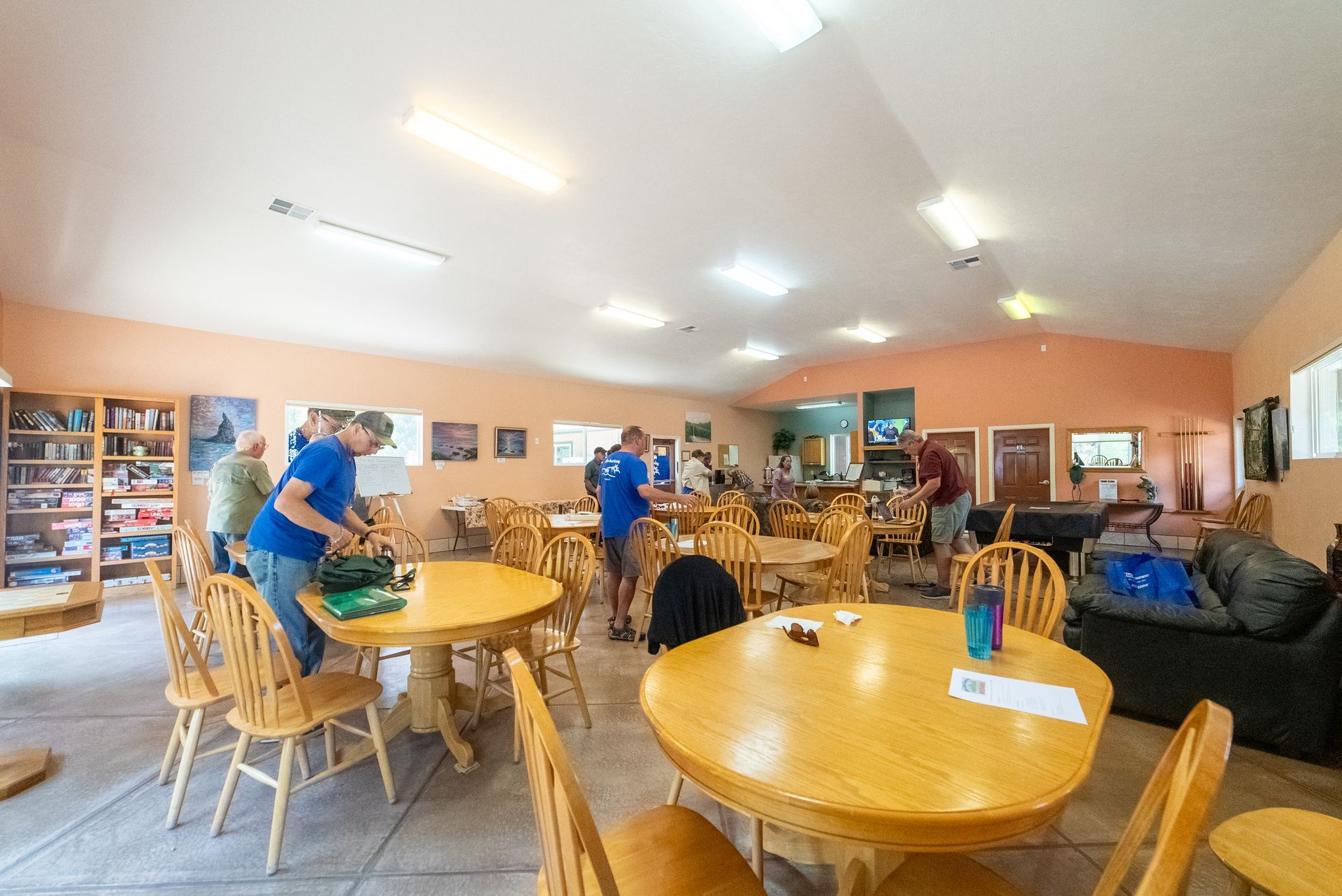 People at tables in a brightly lit room with shelves and couches.