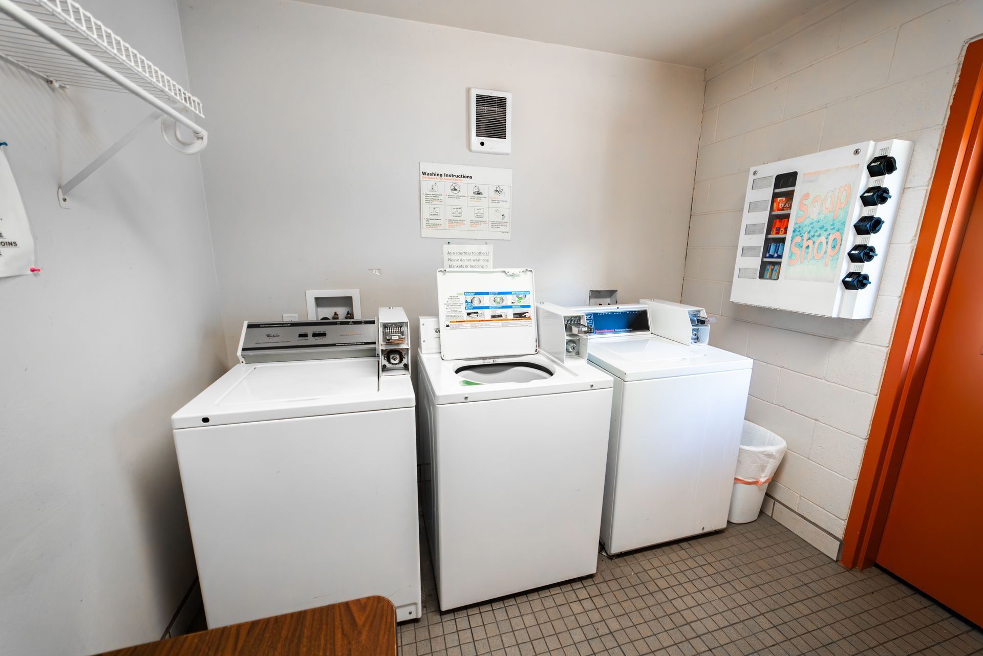Laundry room with three washing machines, a payment panel, and an orange door.