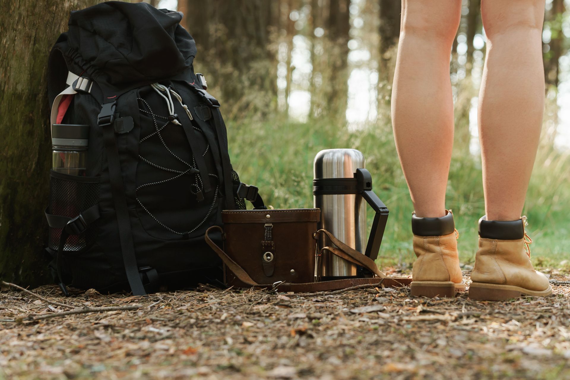 Backpack, boots, and gear at the base of a tree in a forest.