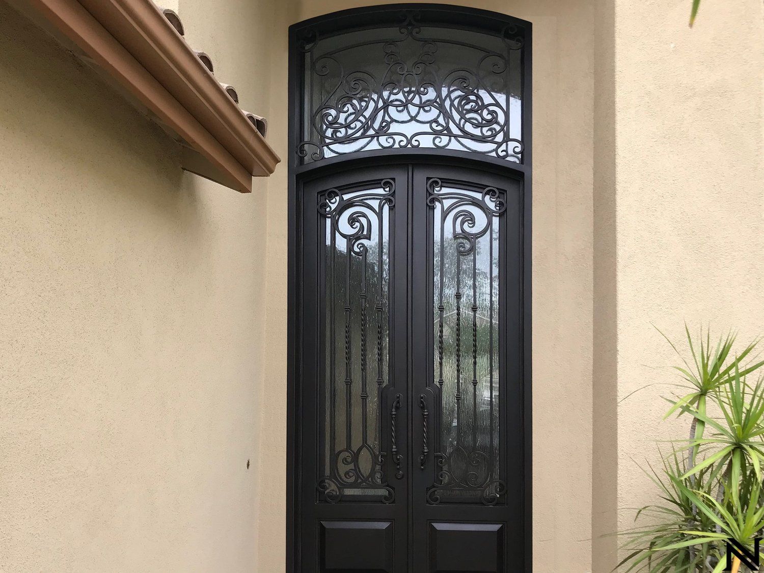 A black door with a wrought iron design is on the side of a building.