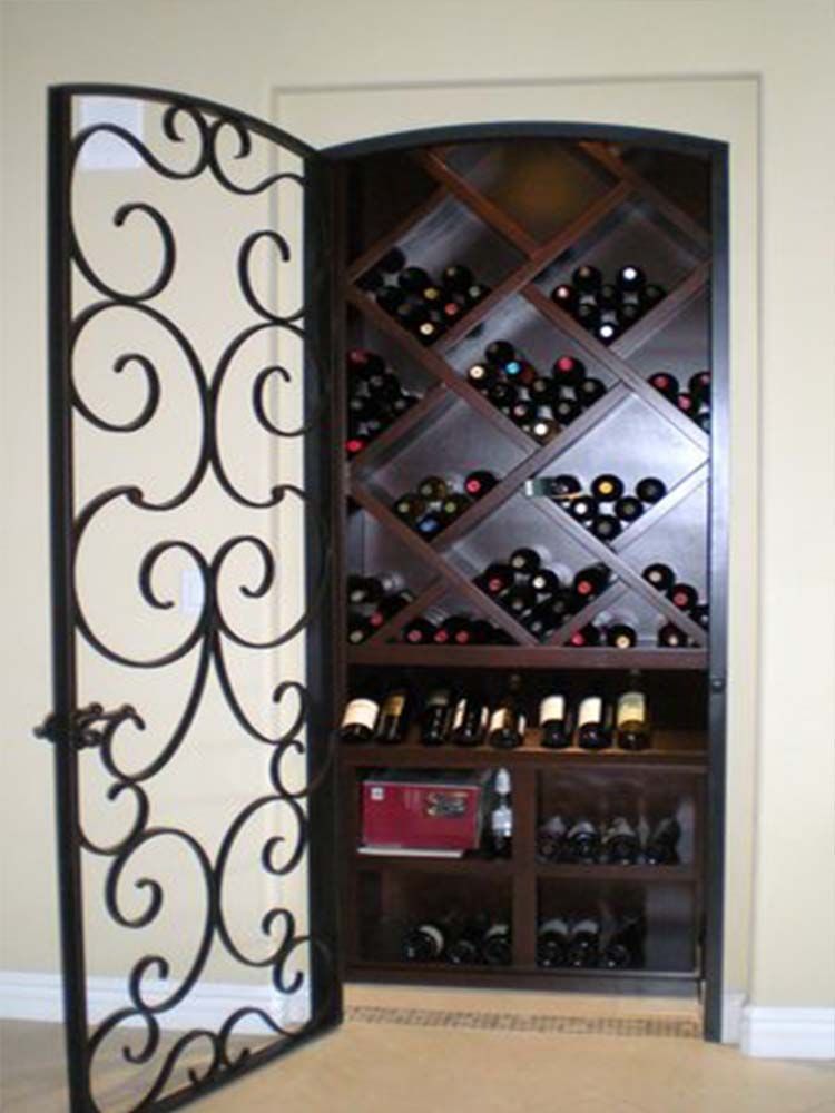 A wrought iron door open to a wine cellar