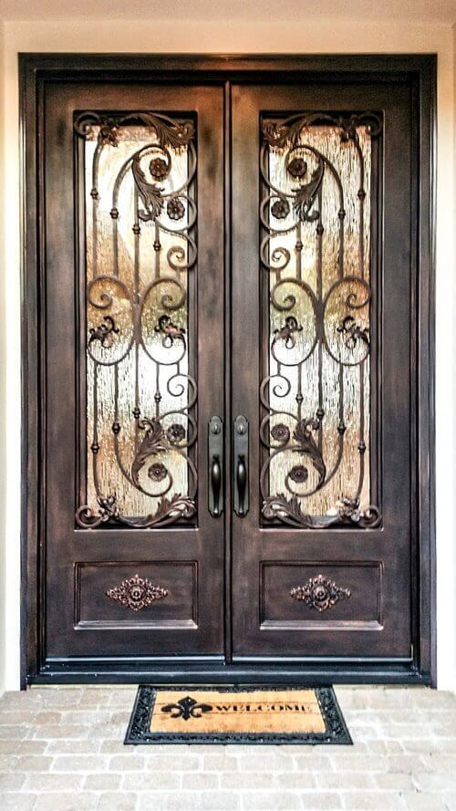 A wrought iron double door with a welcome mat underneath it.