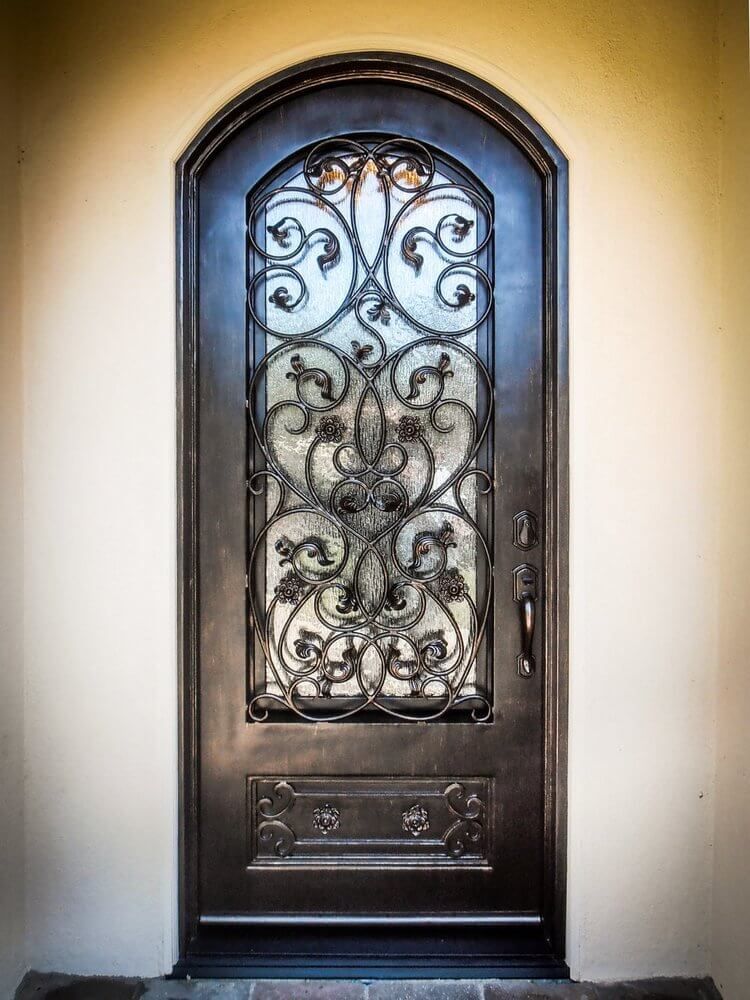 A black door with a wrought iron design on it is on a white wall.