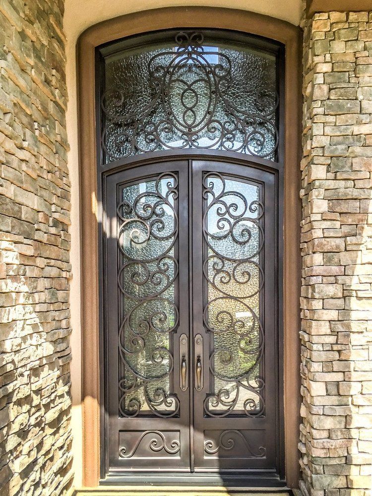A wrought iron door with a stained glass window is on a brick wall.