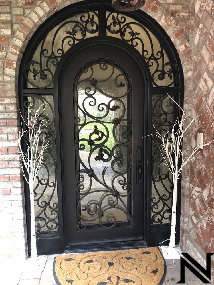 A black wrought iron door with a brick wall behind it.