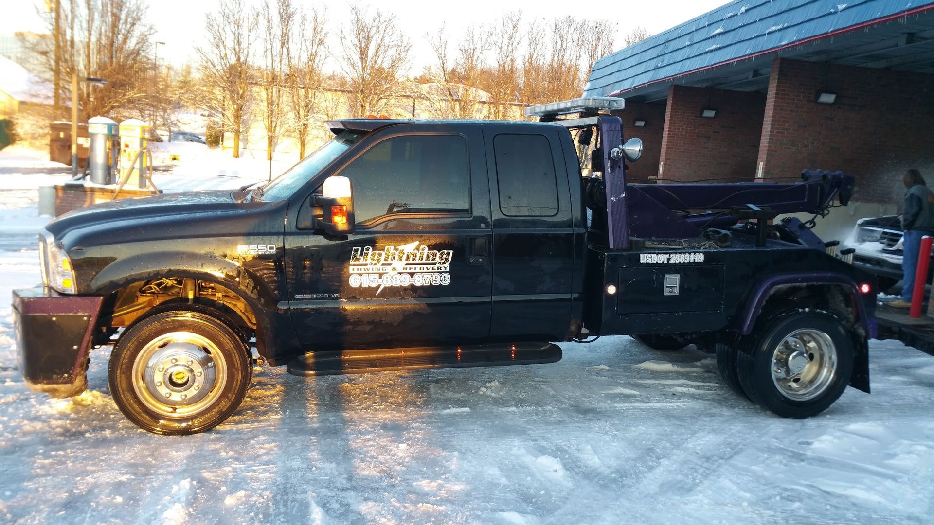 A black tow truck is parked in the snow in front of a building.