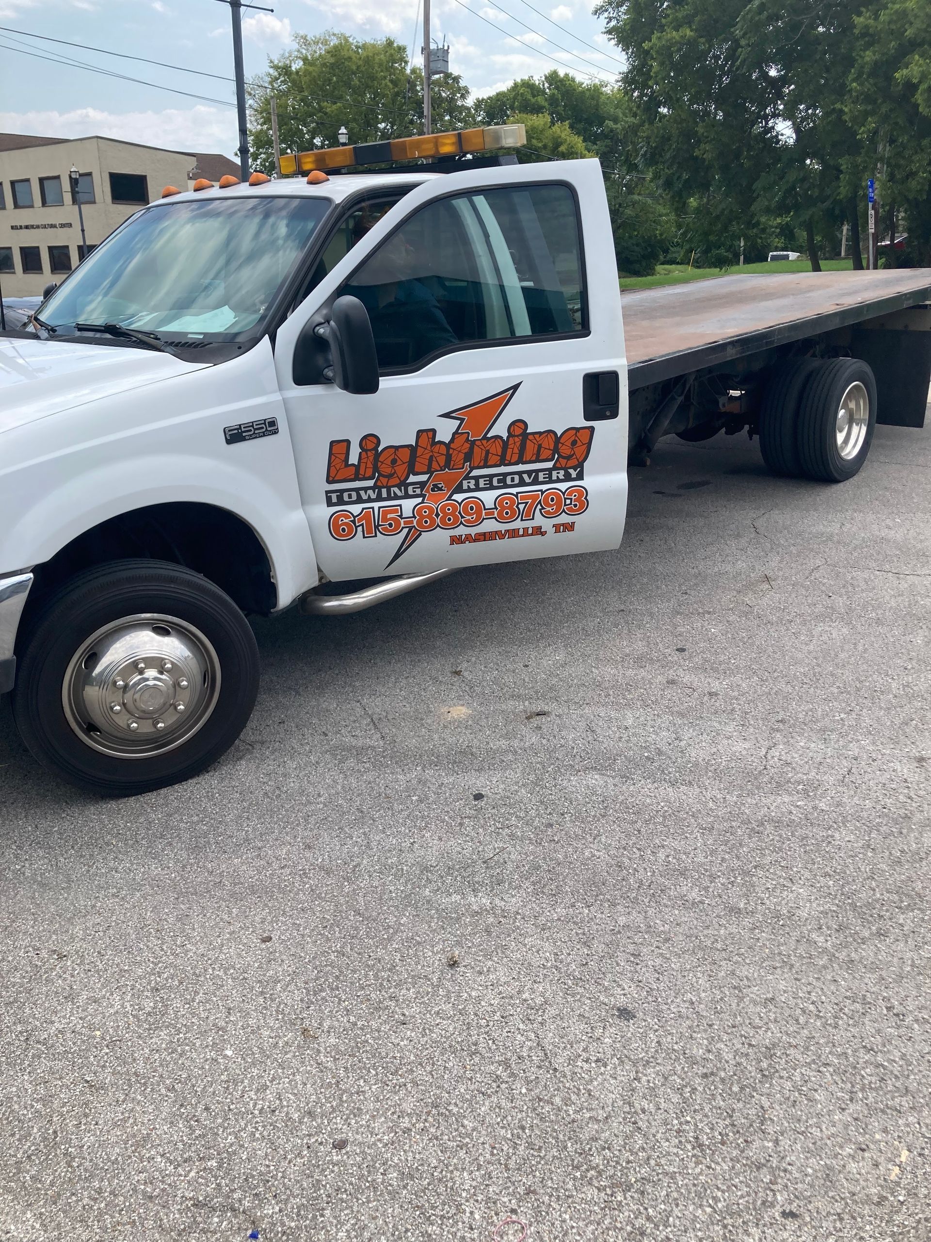 A white tow truck with a flat bed is parked in a parking lot.