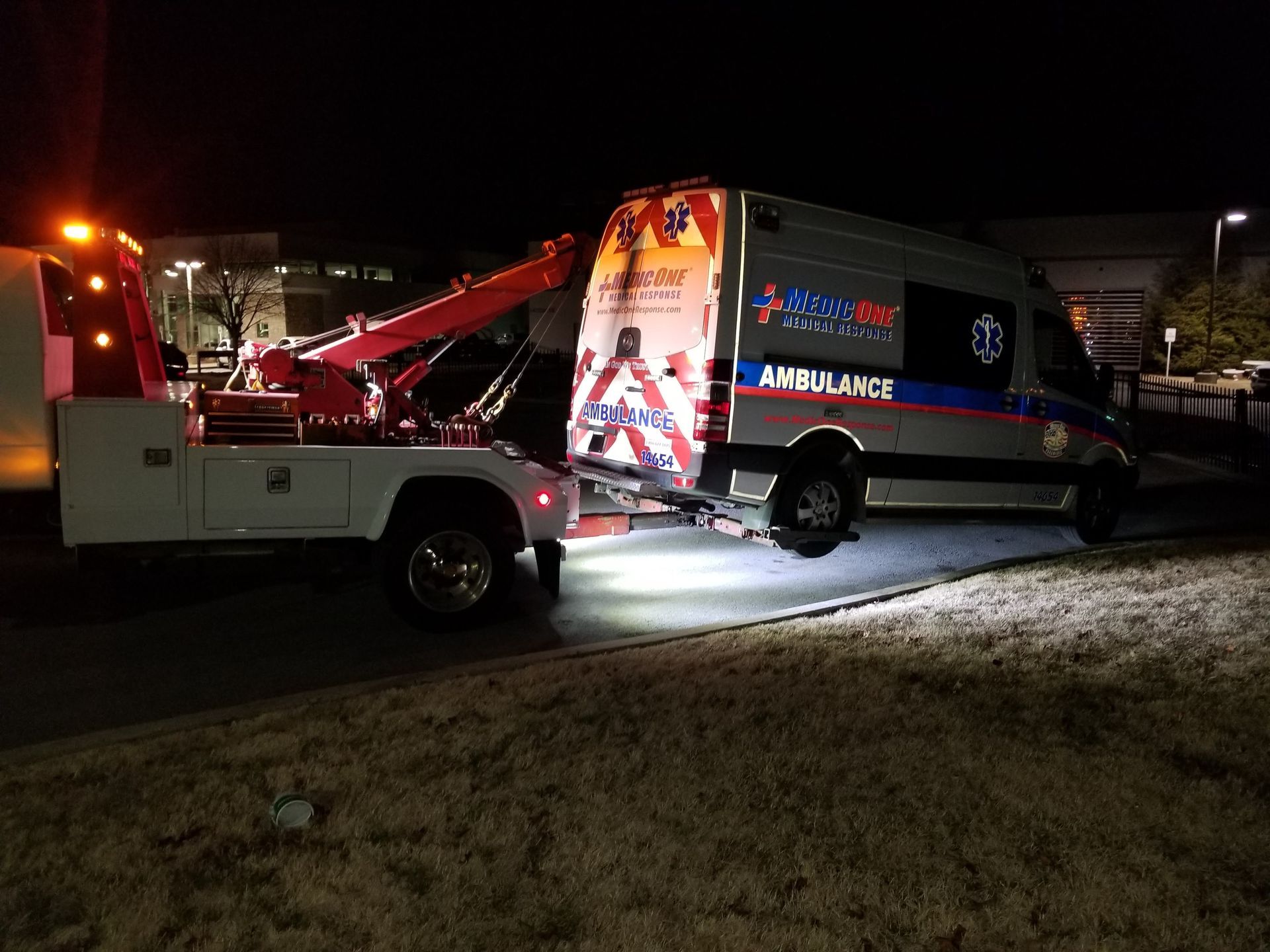 An ambulance is being towed by a tow truck at night.
