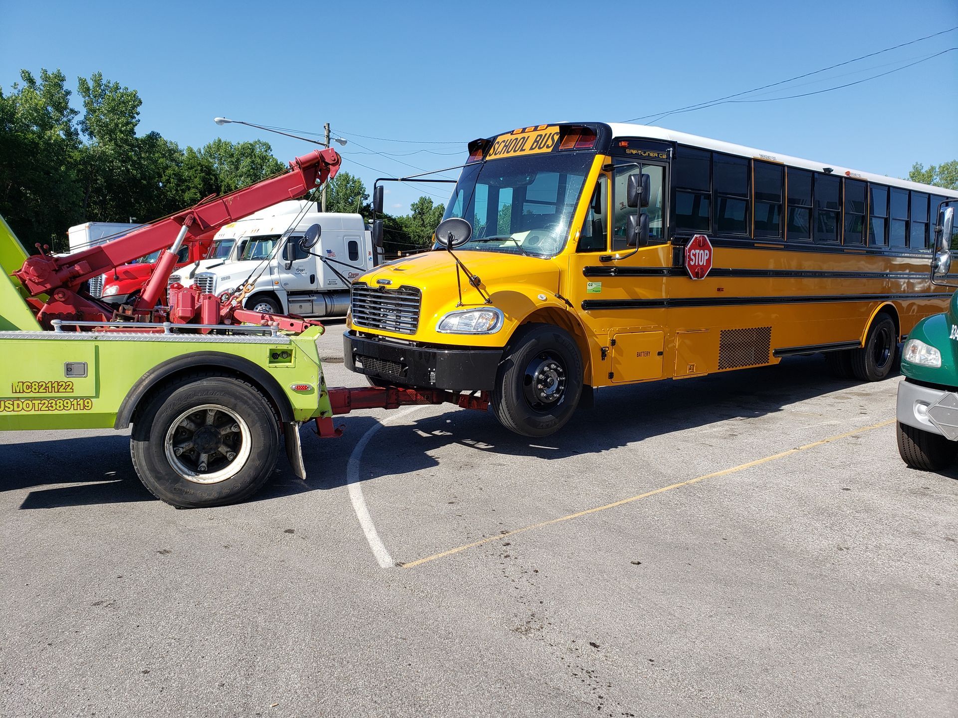 A yellow school bus is being towed by a green tow truck