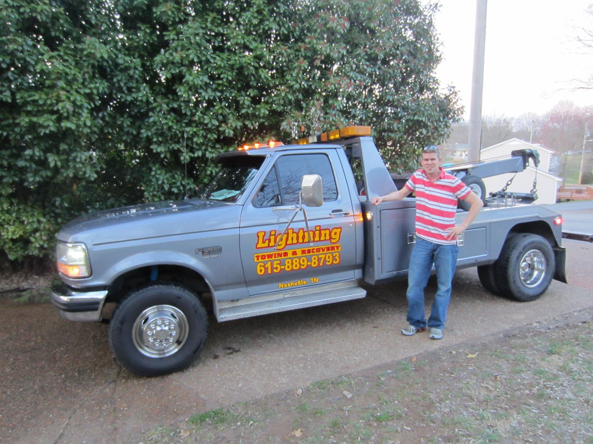 A man standing next to a tow truck that says lightning