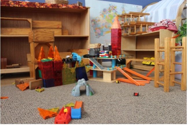 Child's playroom with wooden structures, ramps, and toy cars scattered on the carpet.
