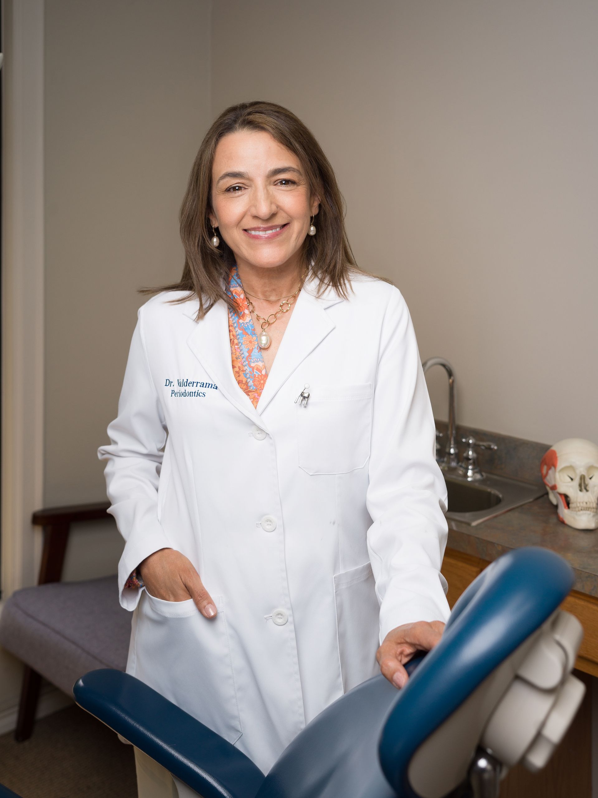 A professional in a white lab coat standing in a dental office next to a patient chair.