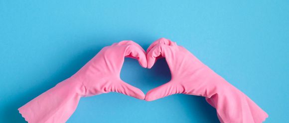Two hands wearing pink rubber cleaning gloves shaped into a heart against a solid light blue background. Two hands wearing pink rubber cleaning gloves shaped into a heart against a solid light blue background.