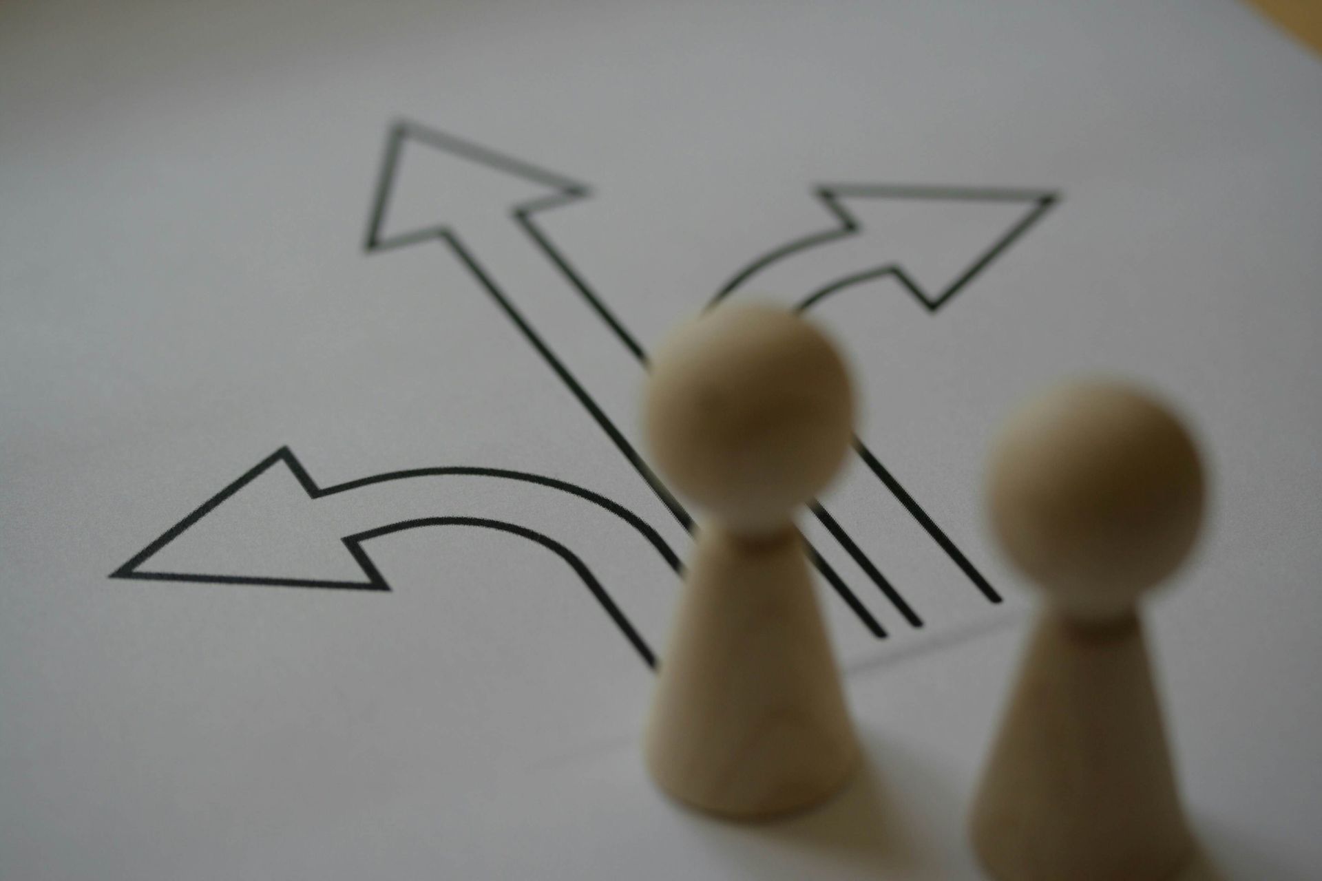 Two wooden figures stand before a drawing of arrows pointing in different directions, representing choices.