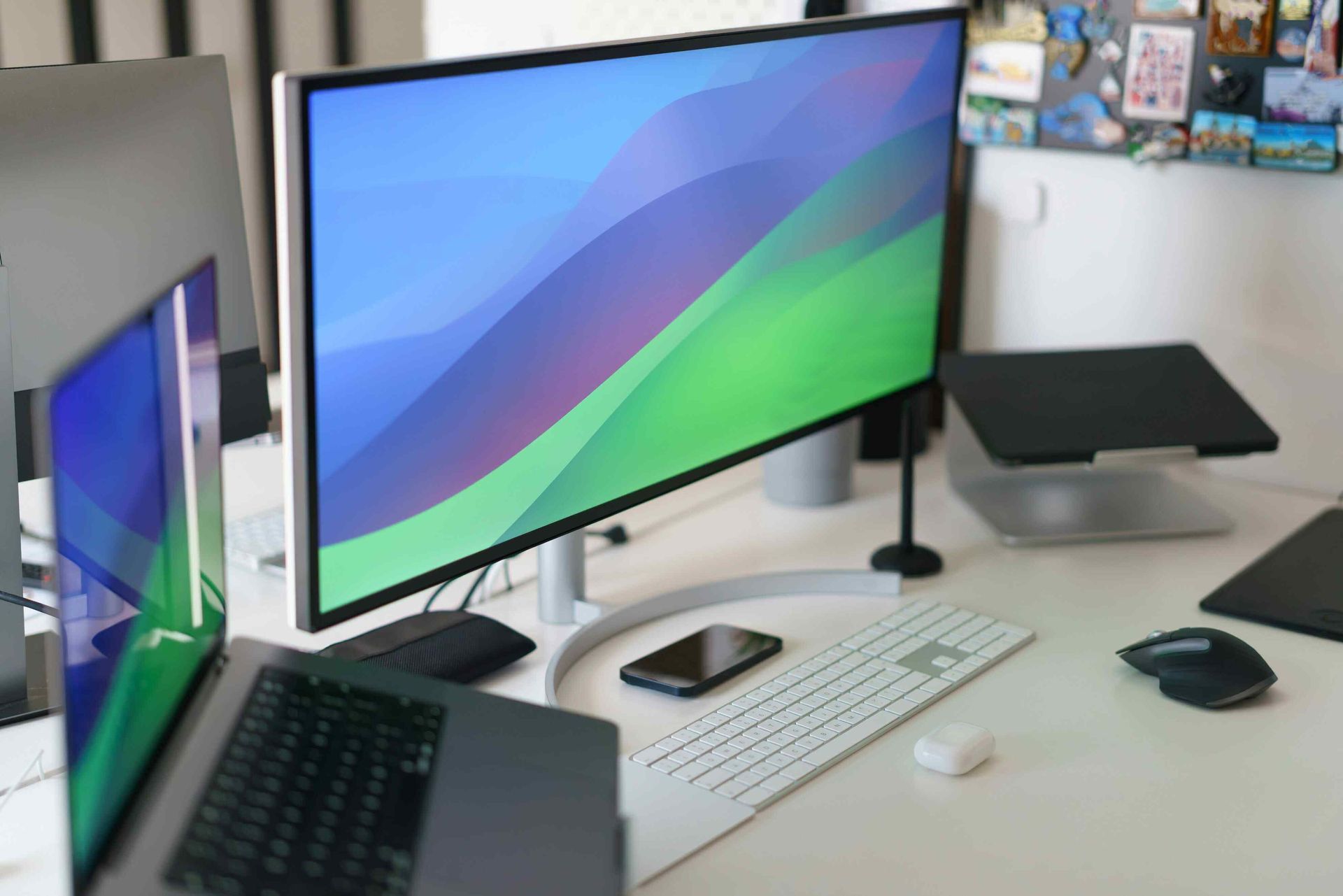 Desk setup with laptop, monitor displaying blue and green abstract wallpaper, keyboard, mouse, and phone.