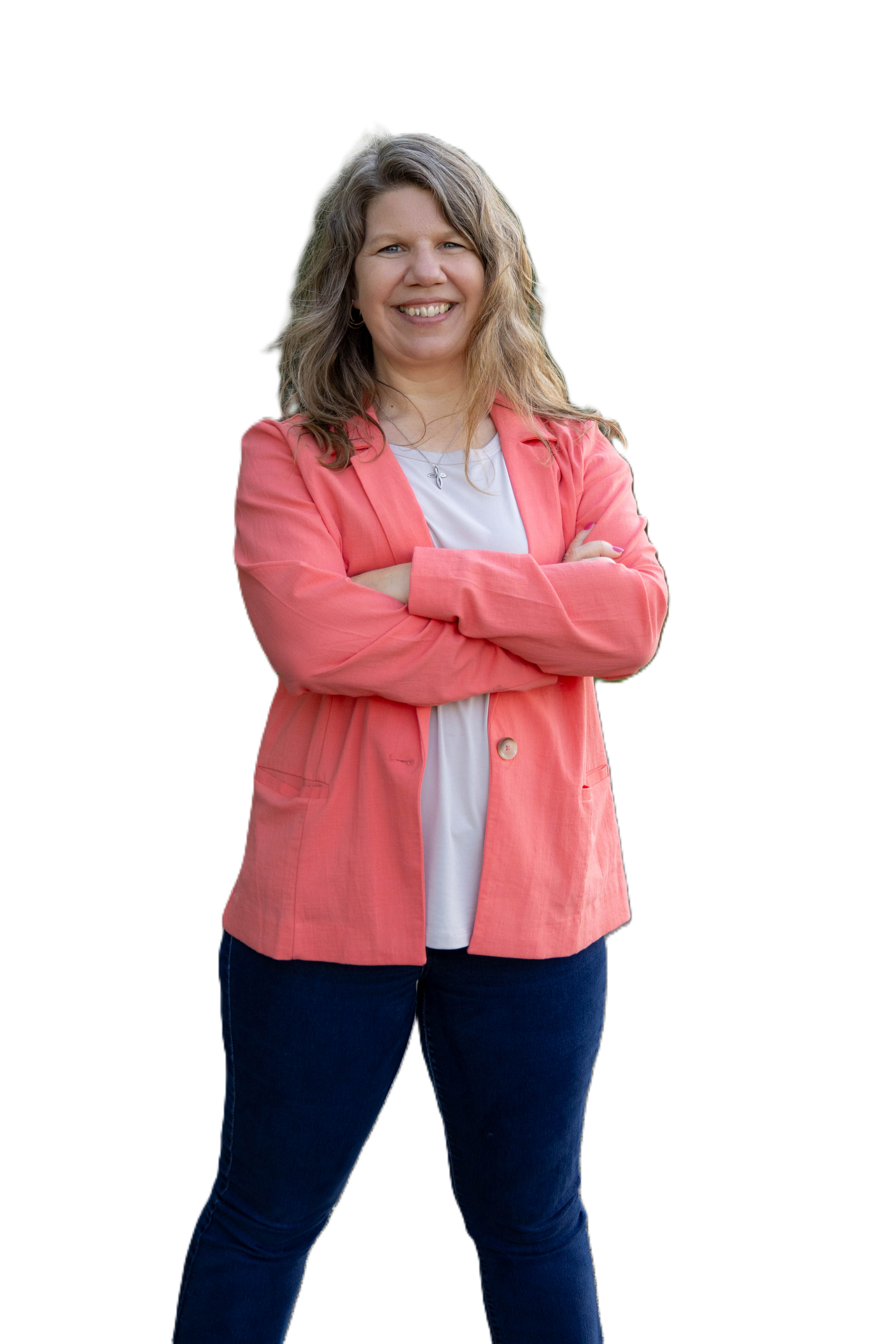 Woman with curly hair, wearing a coral blazer, white shirt, and blue jeans, arms crossed, smiling.