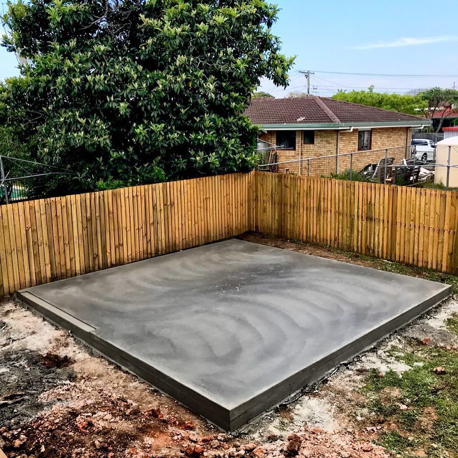 A newly poured, smooth gray concrete slab square, enclosed by a bamboo fence in a residential yard. — Sand & Stone in Mudgeeraba, QLD