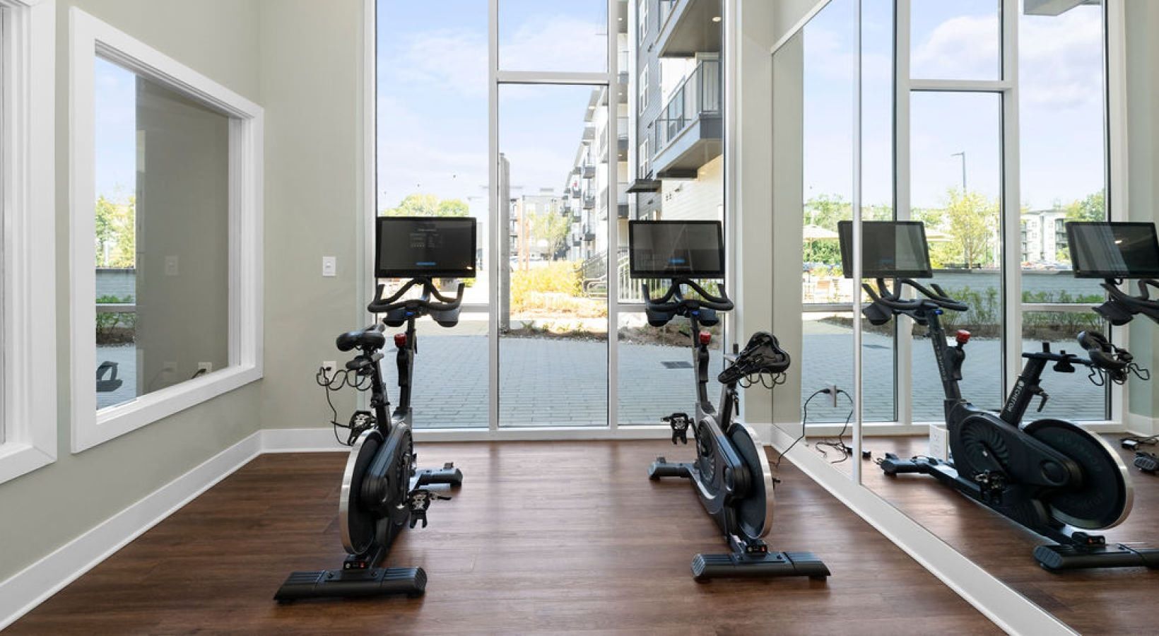 Spin bikes in a brightly lit gym with large windows overlooking an outdoor area. We invite you to visit 1001 Tyvola and take a tour of our apartments with a fitness center in Mecklenburg County.