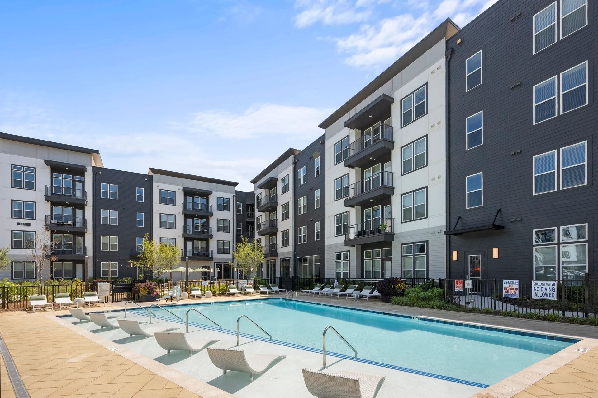 Apartment complex with a swimming pool and lounge chairs on a sunny day. We invite you to take a tour of our luxury apartments with pools in Charlotte, NC at 1001 Tyvola