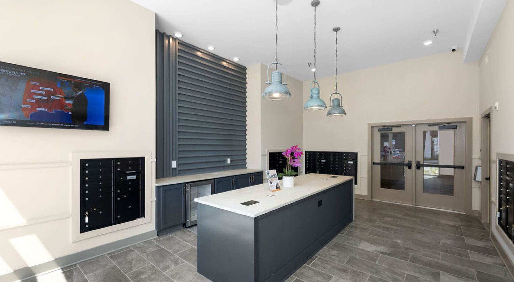 Apartment lobby with mailboxes, counter, TV, pendant lights, and double doors. Gray, white, beige. We invite you to visit 1001 Tyvola and take a tour of our pet-friendly, 2-bedroom apartments in Charlotte, NC.
