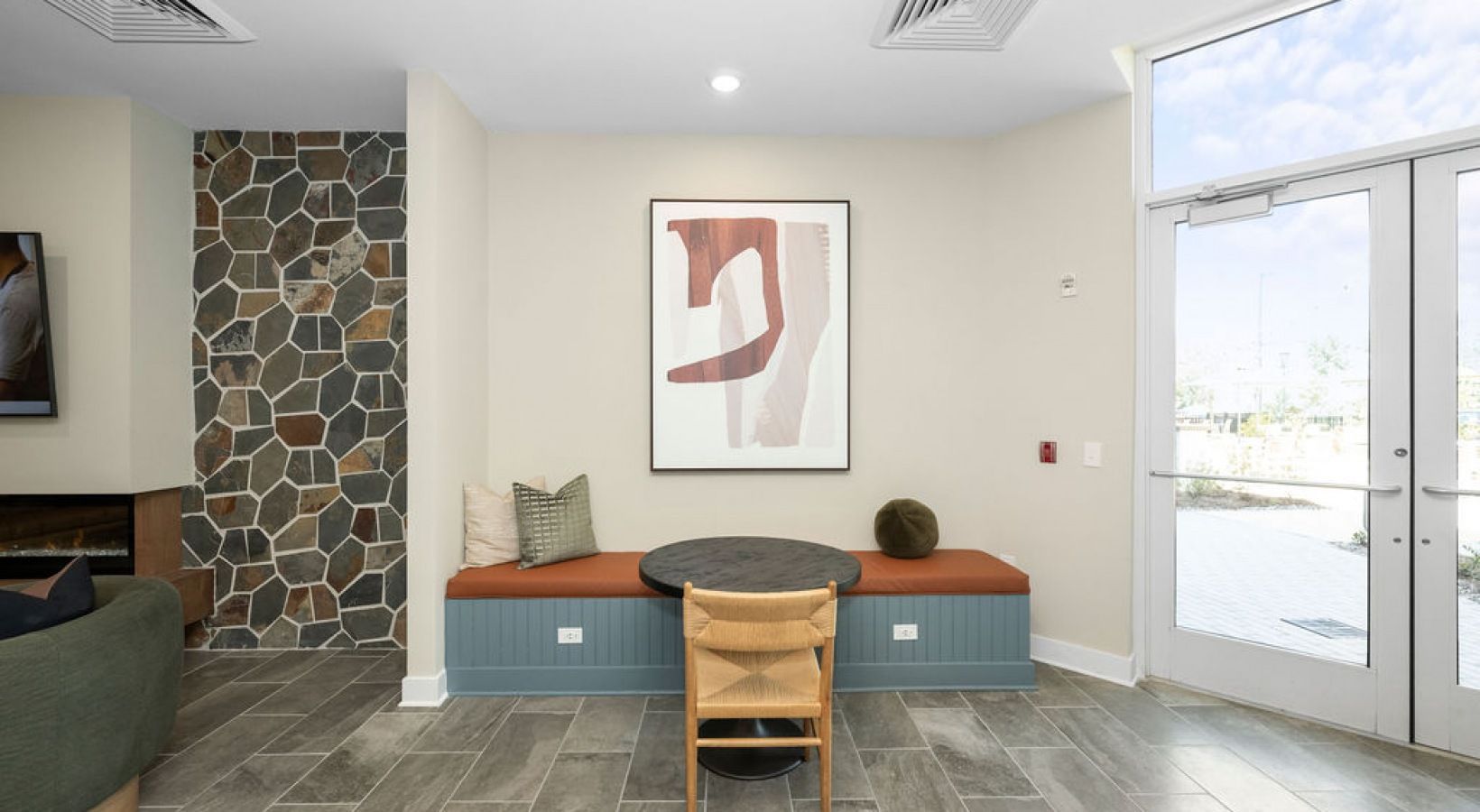 A modern room with a stone accent wall, bench seating, art, and a round table near double doors. We invite you to visit 1001 Tyvola and take a tour of our apartments near Tyvola Station in Charlotte. 