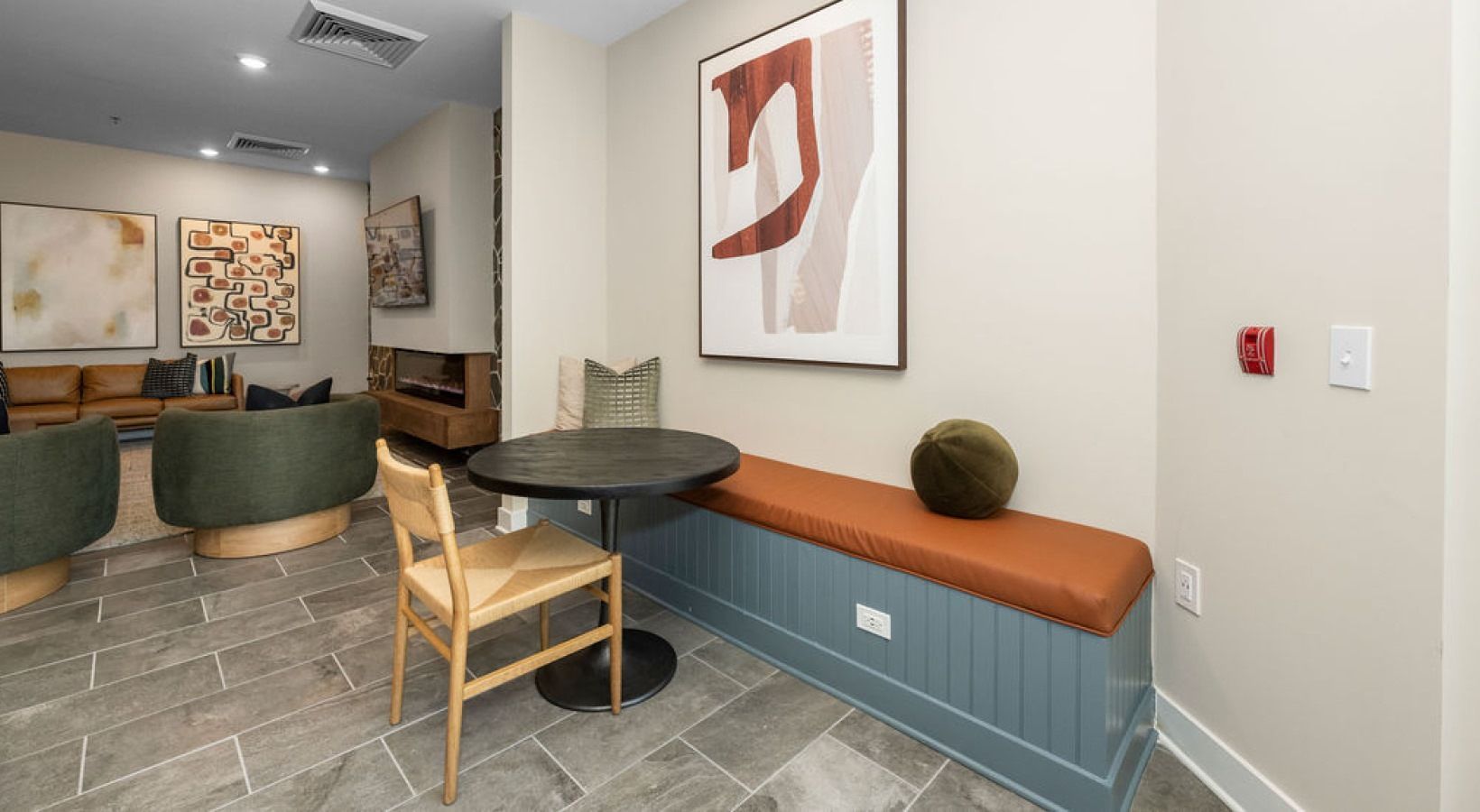 Cozy lounge area with round table, bench, art, and two green chairs. Gray tile floor, light walls. We invite you to visit 1001 Tyvola and take a tour of our apartments near Latta Park in Charlotte.