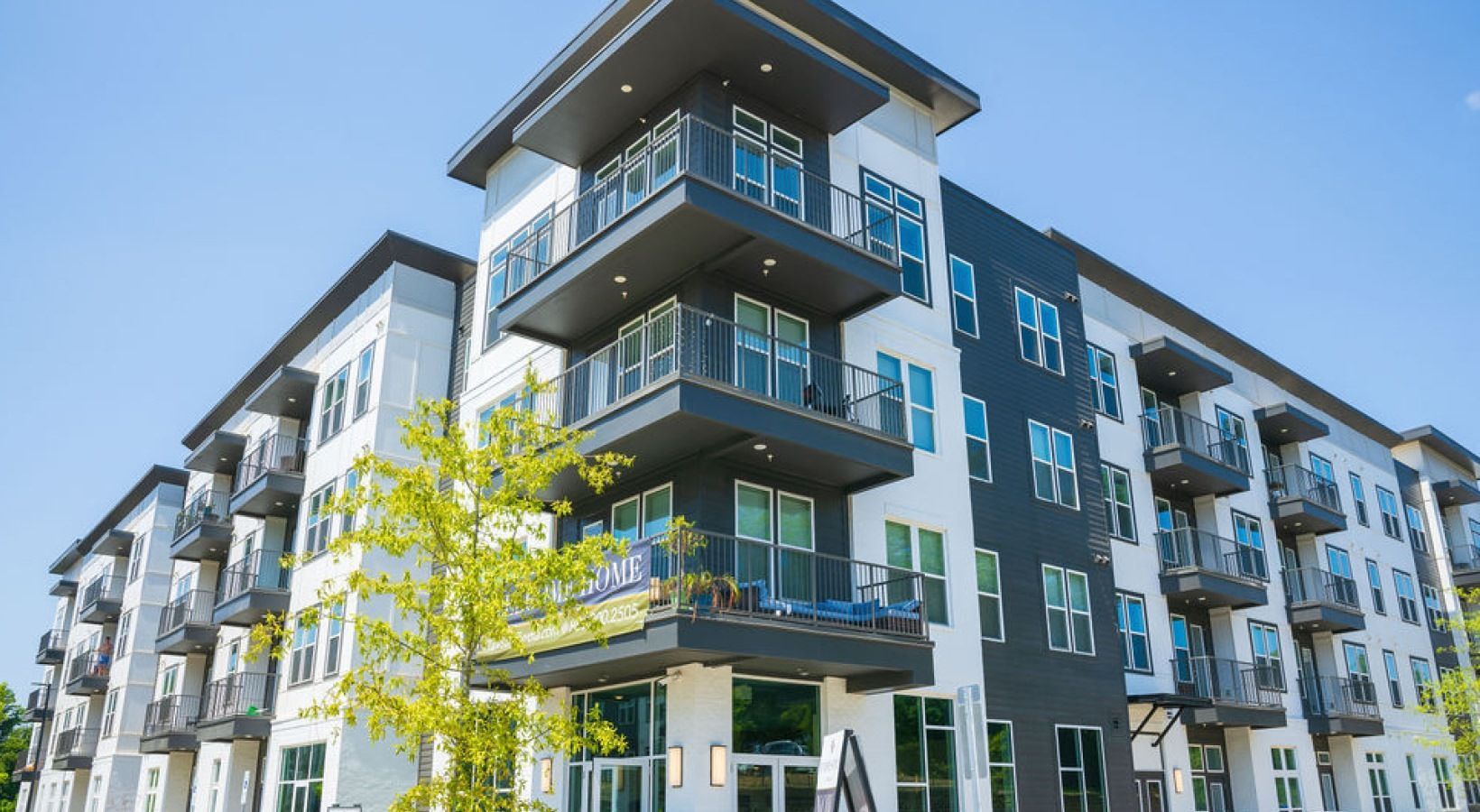 Modern apartment building with balconies, gray, black, and white facade, blue sky background.