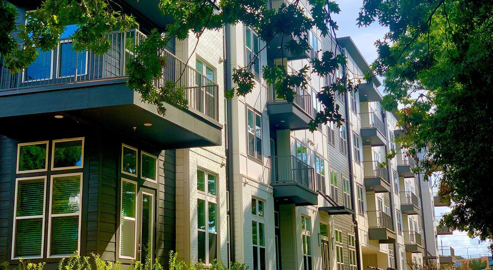 Modern multi-story apartment building with balconies, trees framing the view. We invite you to visit 1001 Tyvola and take a tour of our apartments in Charlotte, NC.