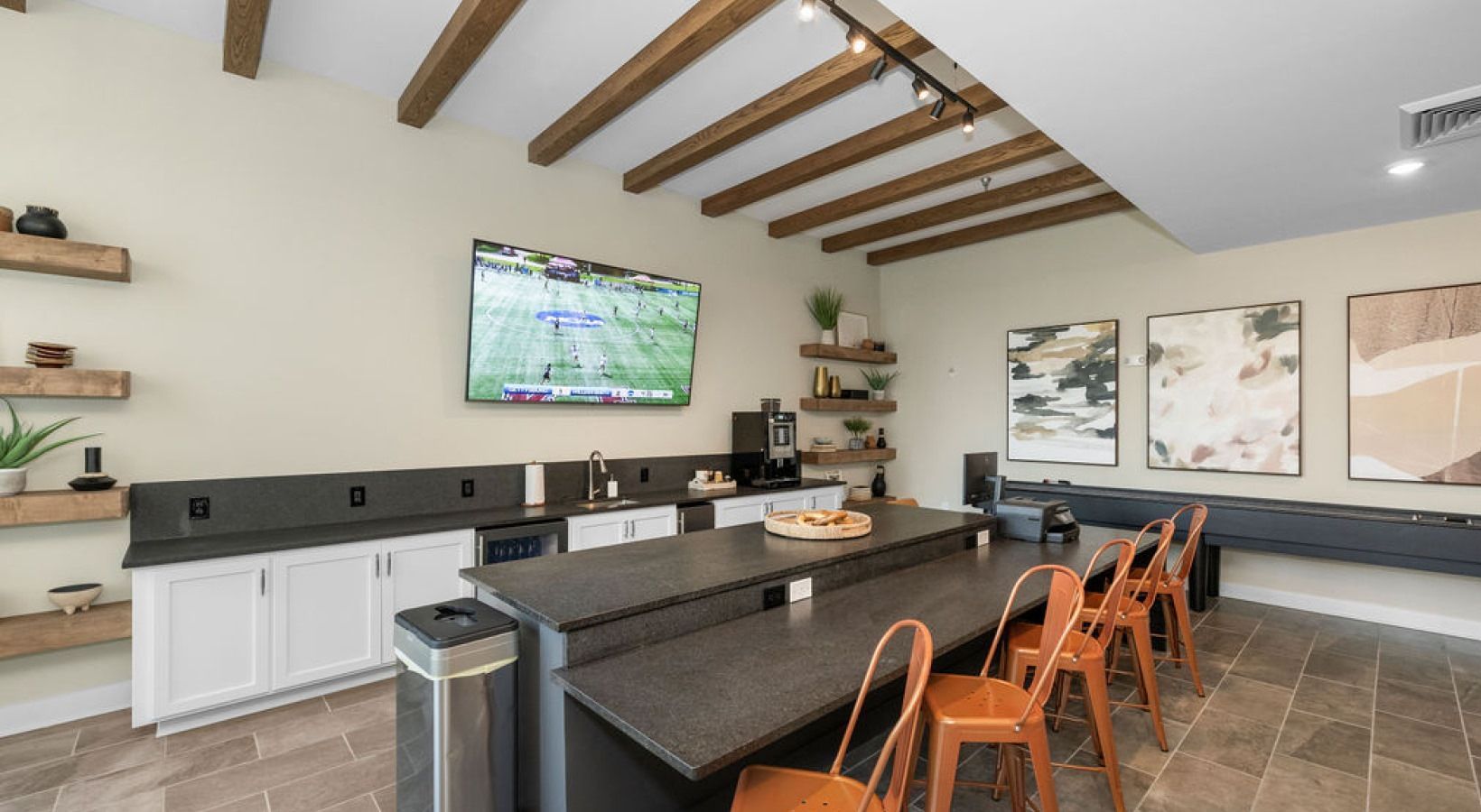 Interior shot of a communal kitchen area with a TV, a long counter with stools, and wooden beams on the ceiling. We invite you to visit 1001 Tyvola and take a tour of our apartments near Freedom Park in Charlotte, NC.