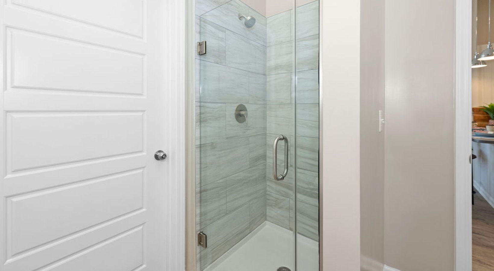 Glass shower enclosure with gray tile, white door, and neutral walls. We invite you to visit 1001 Tyvola and take a tour of our Charlotte apartments near CLT Airport Overlook.