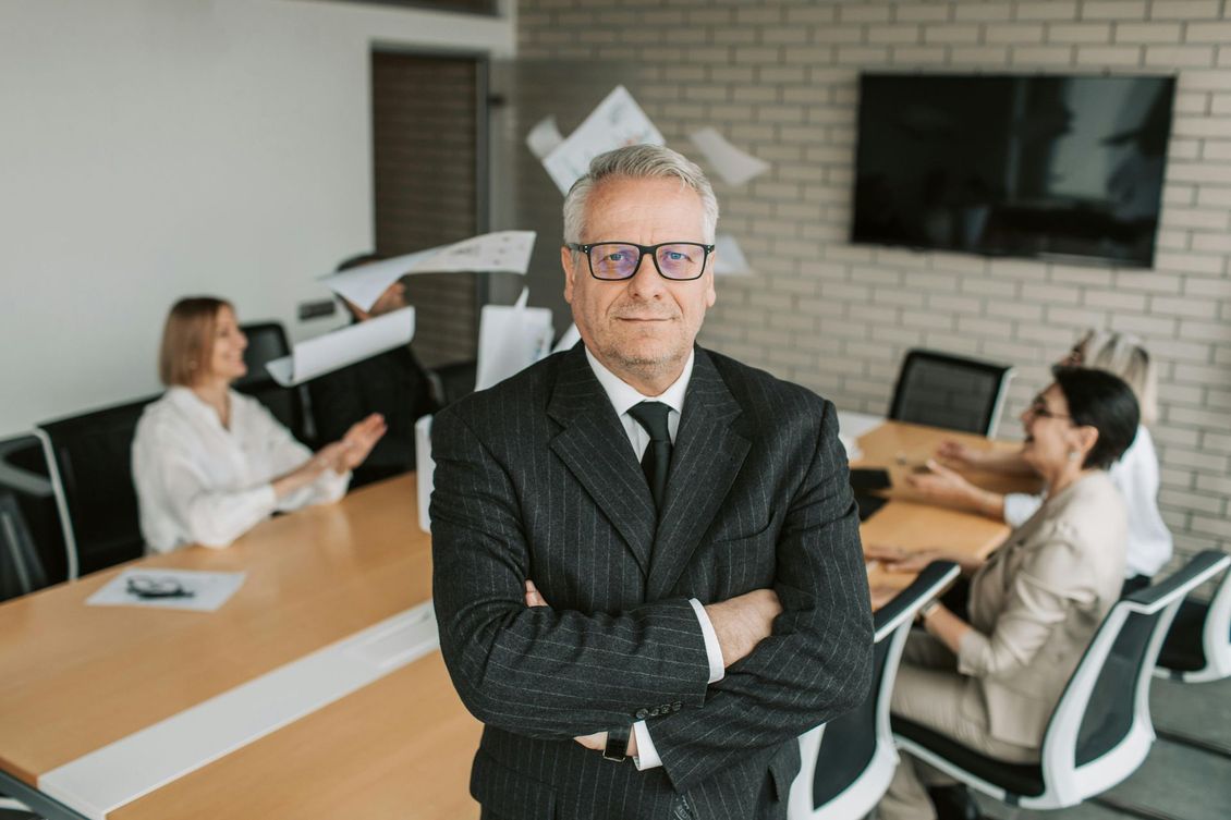 Business meeting in a modern office, with a suited man standing in front of colleagues at a conference table.