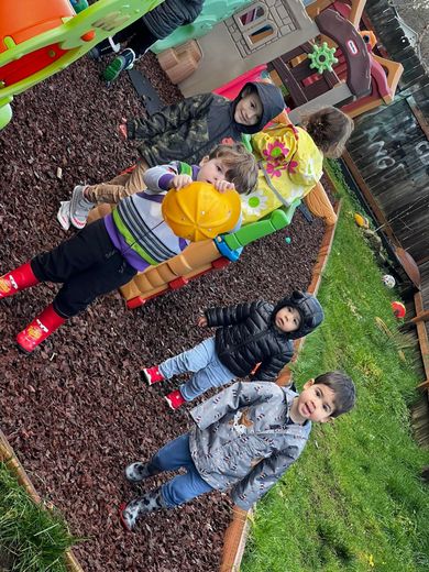 Children playing on wooden playground structure with slides and climbing wall in grassy area.