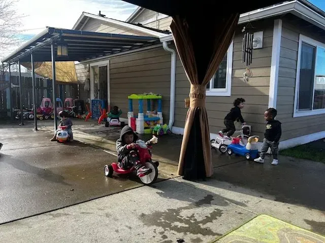 Children playing with ride-on toys on a patio outside a building.