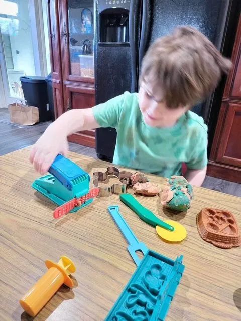 Boy playing with colorful playdough tools and clay on a table.