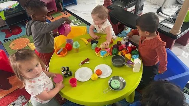 Children playing with toys around a green table in a brightly-lit room.