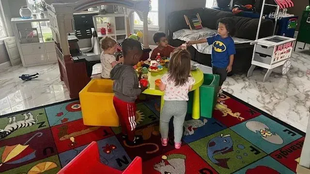 Children gathered around a table playing, on a colorful rug.