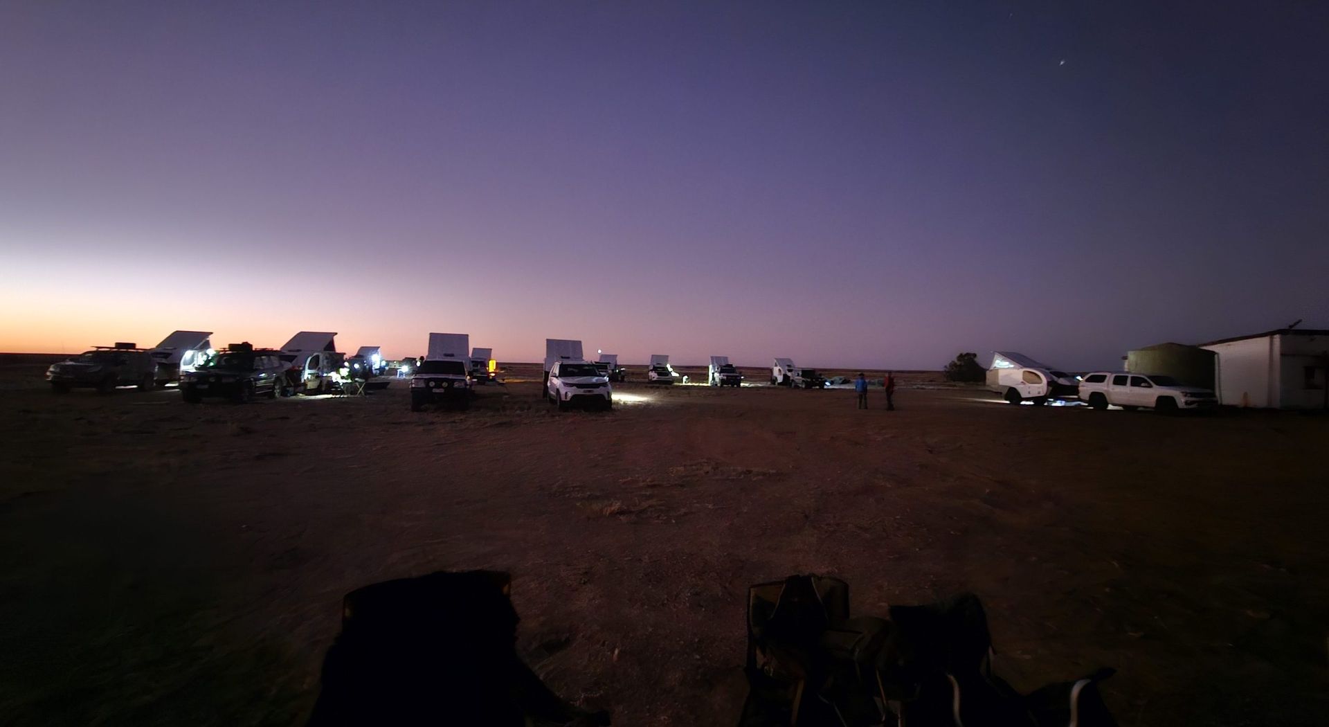 A group of parked SUVs and campers in a vast, open landscape under a twilight sky with a colorful horizon.