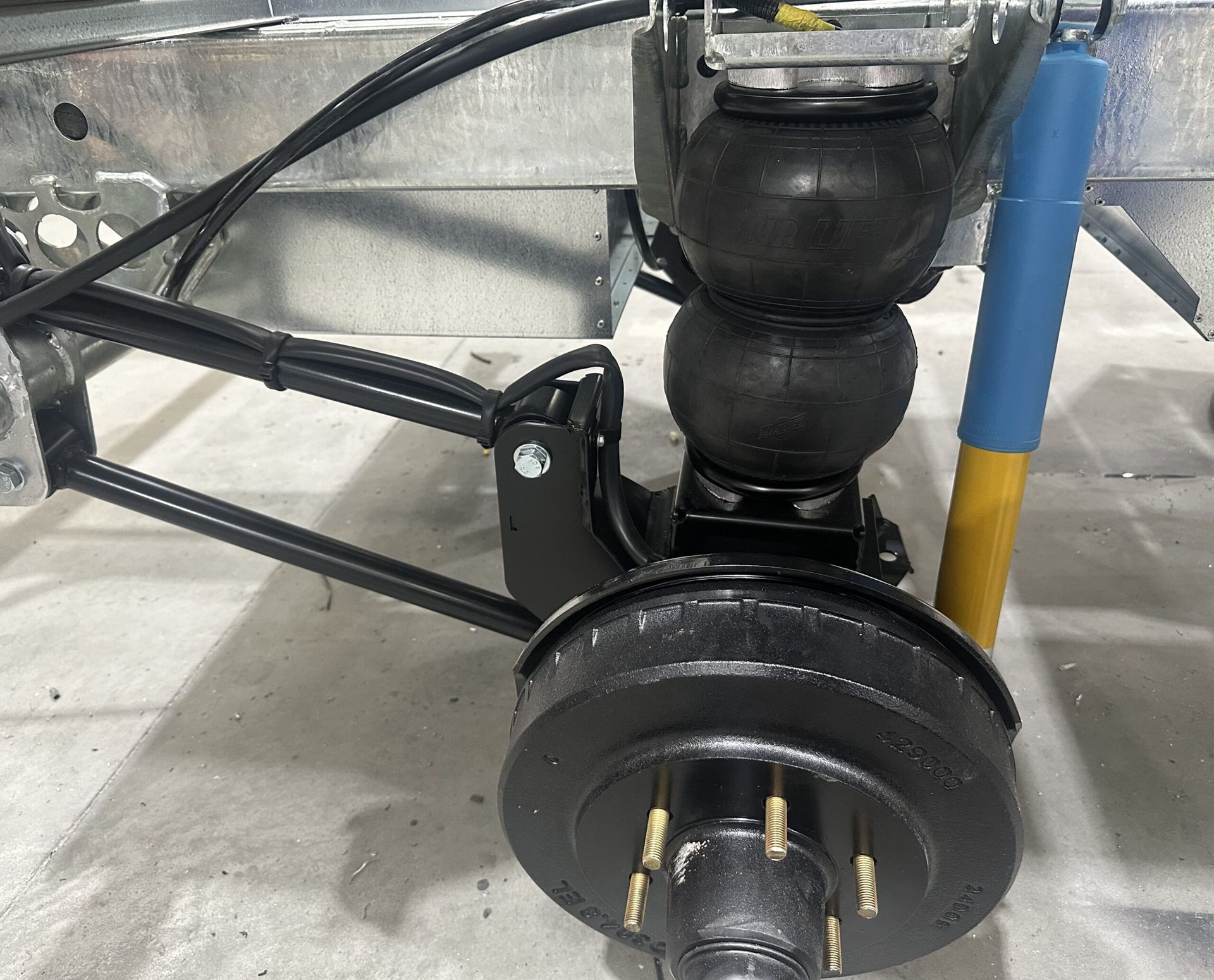 Close-up of a trailer's air suspension system featuring a black air bag, a blue and yellow shock absorber, and a hub.