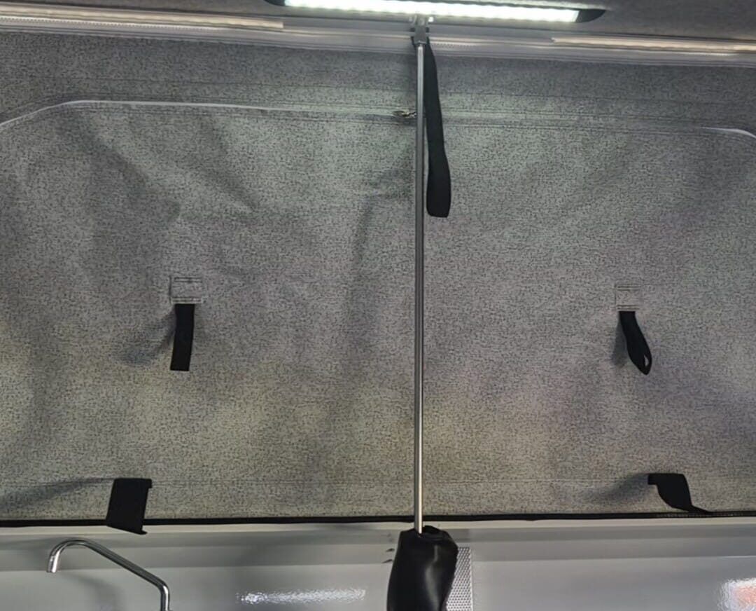 A grey, padded interior wall panel with four black pull straps and a central metal pole, viewed under a bright LED light.