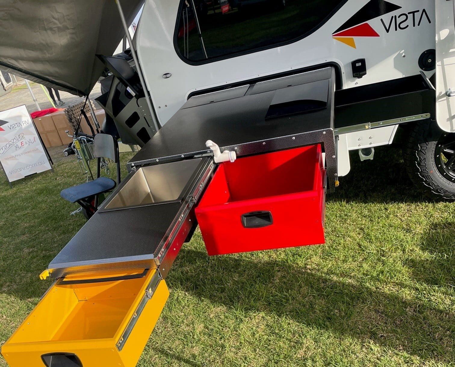 A Vista camper trailer with an extended slide-out outdoor kitchen featuring a yellow drawer, a red bin, and a sink.