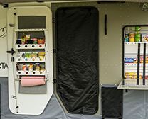 A white storage unit mounted on a camper door, featuring shelves with supplies, a paper towel roll, and side wall shelving.