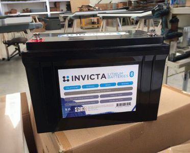 An Invicta lithium battery with a Bluetooth logo sitting on a cardboard box in a warehouse setting.