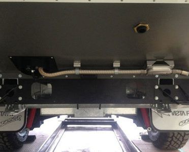 An underside view of a vehicle chassis showing a metallic exhaust pipe running horizontally above the rear bumper.