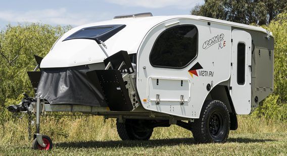 A white off-road camper trailer parked in a grassy field under a sunny sky.