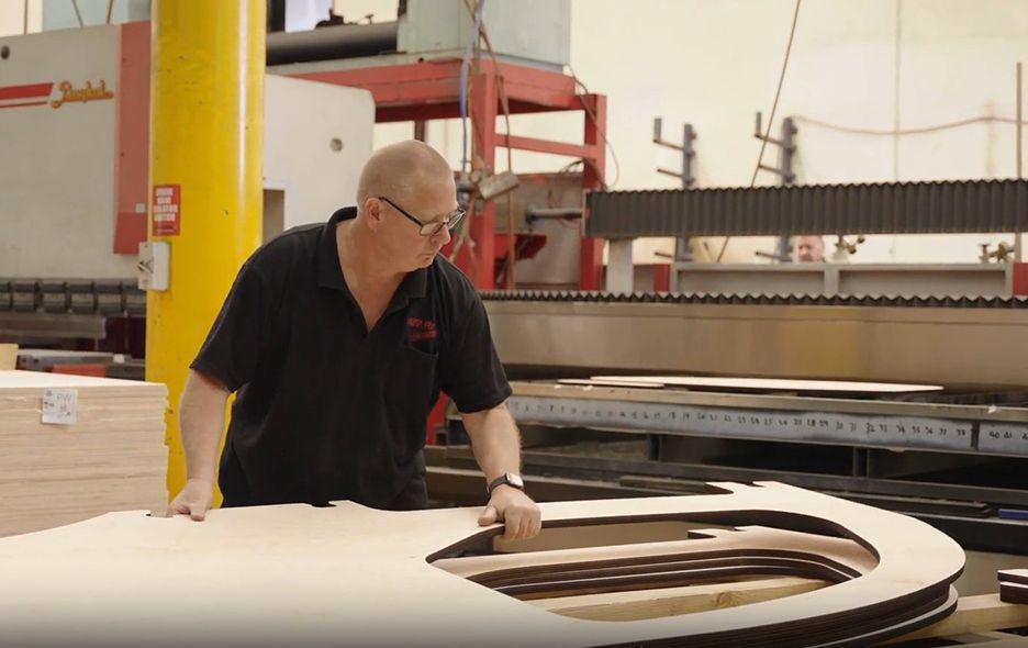 A person in a black polo shirt operates a large industrial wood-cutting machine in a workshop.
