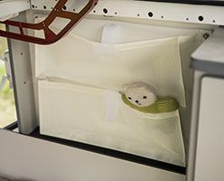 A cream-colored, two-tiered fabric hanging organizer is mounted under a cabinet, holding a small plush toy.