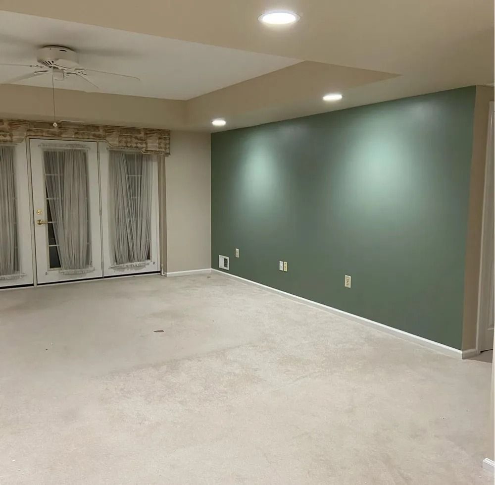 An empty room with beige carpet, double doors, and a green accent wall with recessed lighting.