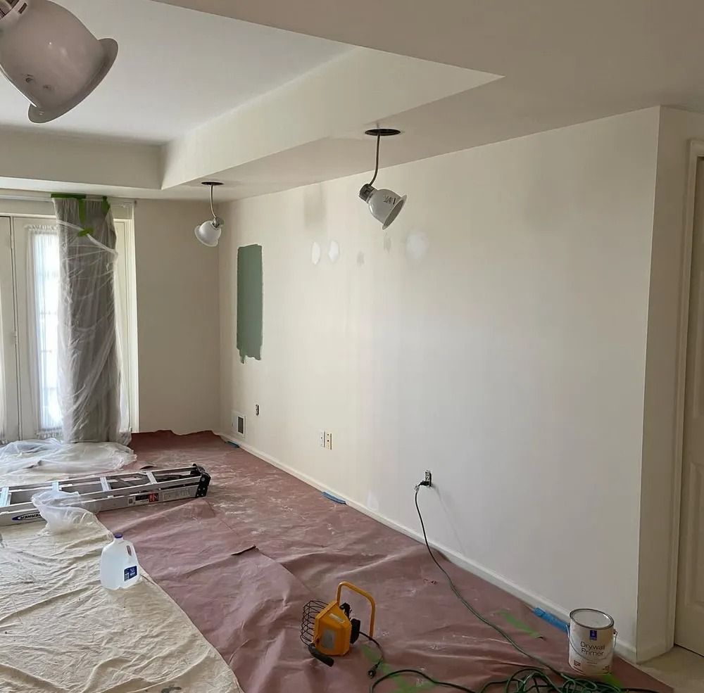 A room being painted, with a red drop cloth covering the floor. Unfinished walls are white, and there are paint cans and tools.