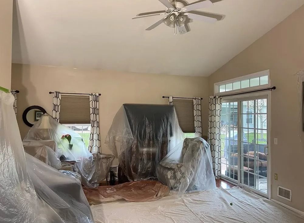 A living room being prepared for painting, furniture covered in plastic sheeting to protect it.