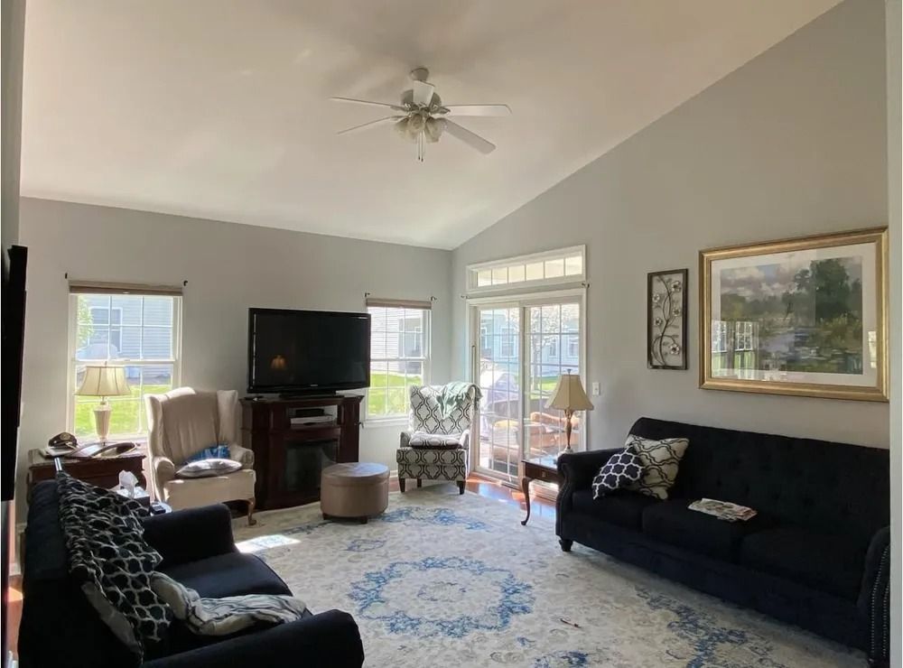 Living room with gray walls, black couches, a floral rug, and a television. A sliding glass door leads to an outdoor patio.